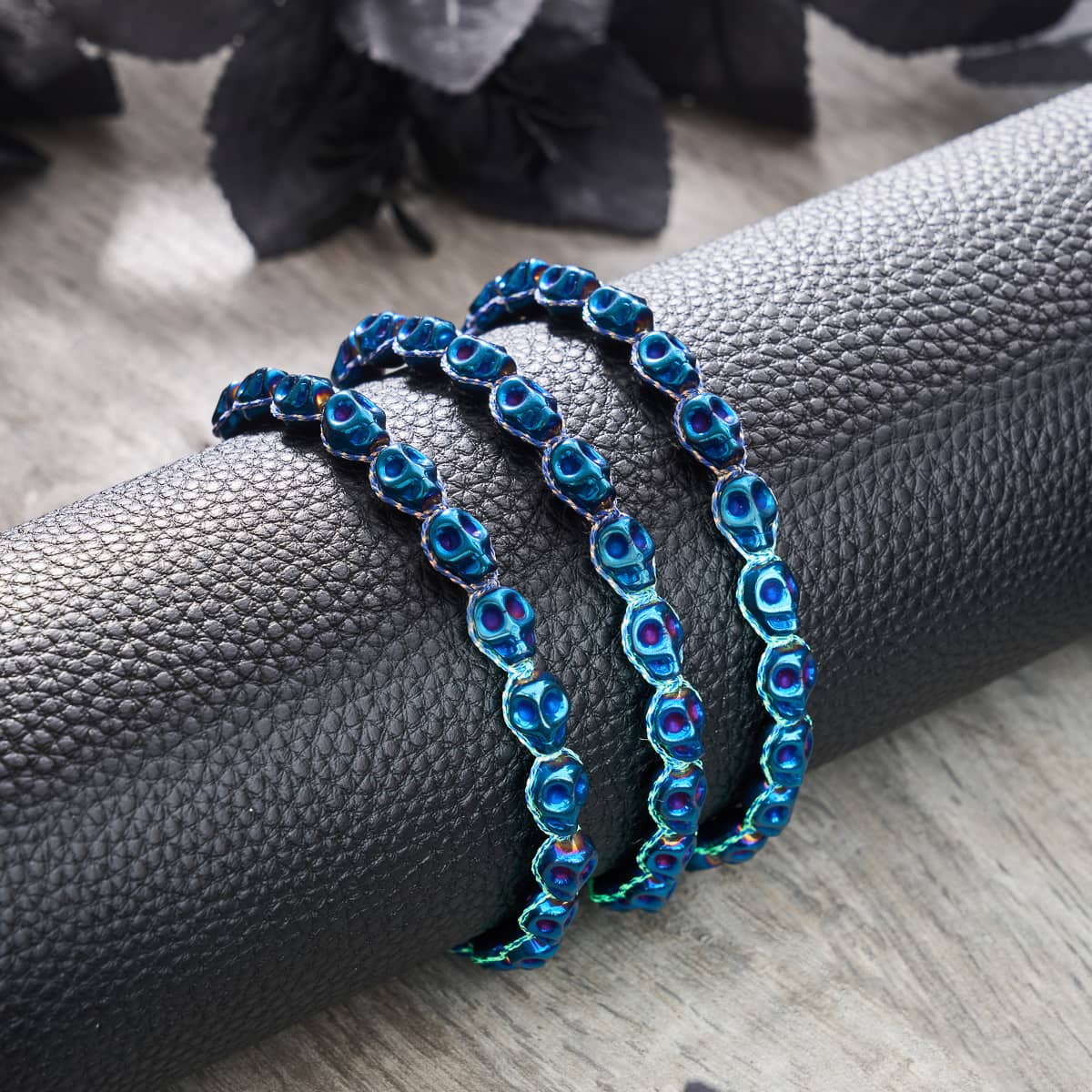 Midnight Mirage cobalt skull beads strung on blue GloWeave macrame bracelet displayed on black textured holder by NOGU